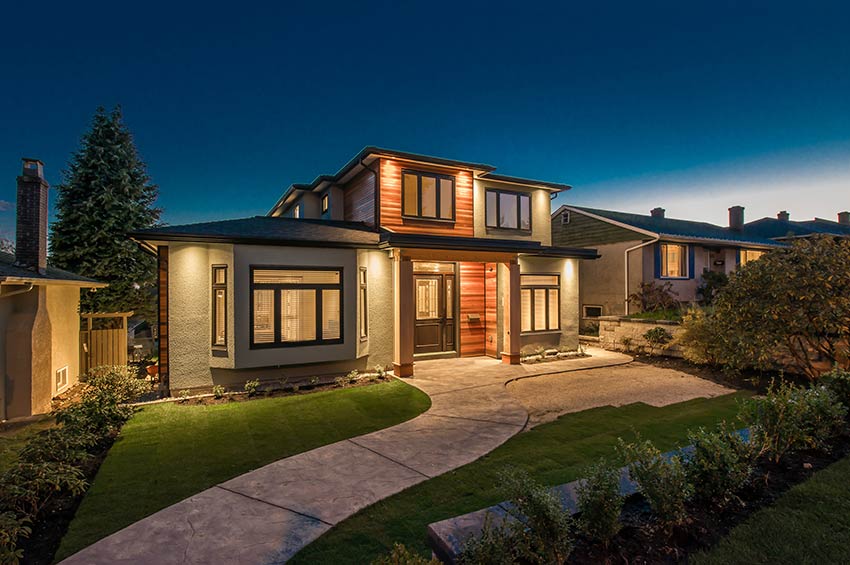 Modern suburban house at dusk with exterior lighting that illuminates a concrete pathway and lawn