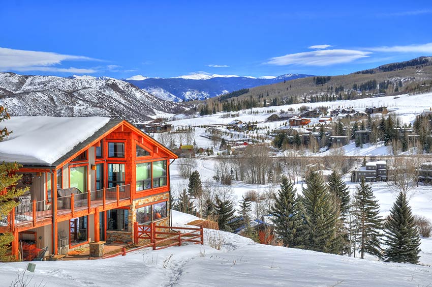 Elegant resort style mansion in winter overlooking other properties and snow-capped mountains